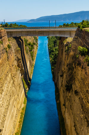 Vertical view of the Corinth Canal in Greece with deep turquoise water, high cliffs, and a road bridge crossing above, captured on a sunny summer day.の写真素材