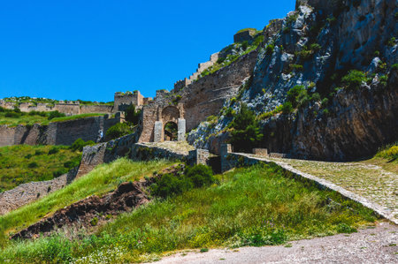 The main stone entrance and medieval walls of Acrocorinth fortress in Corinth, Greece, stand tall under a vivid blue sky, showcasing the siteâs ancient military architecture.の写真素材