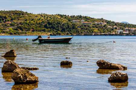 Traditional fishing boat floats peacefully in the turquoise waters of Lake Vouliagmeni, Corinth, Greece. Scenic hills and stone foreground complete the tranquil summer setting.の写真素材