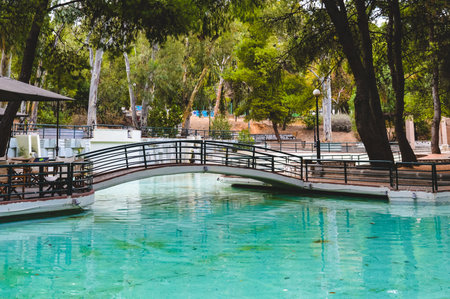 Small pedestrian bridge over turquoise pond at Alsos Papagou in Athens, Greece.の写真素材
