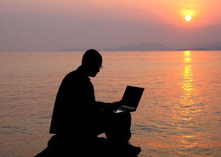 The man with the laptop and a decline on the sea.の写真素材