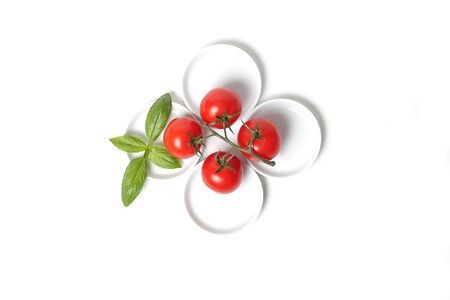 Four tomatoes  with basil leaf on platesの写真素材