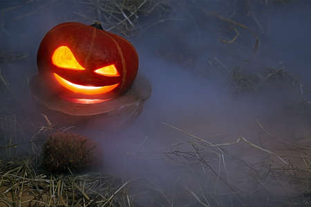 Halloween pumpkin in smoke stands in hay on a wooden stand. Near forest cones.の写真素材
