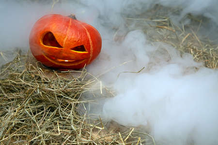 Halloween pumpkin in smoke stands in hay on a wooden stand.の写真素材