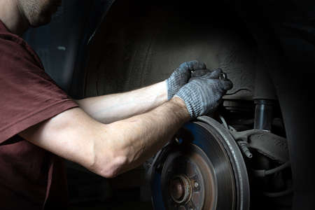A mechanic in the service center checks the suspension of the car. Performs seasonal wheel replacement.の写真素材
