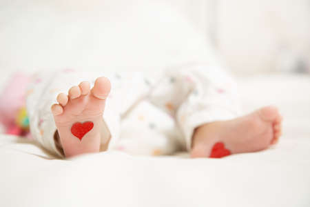 Baby foots with hearts on their feet. A newborn baby is lying on the bed.の写真素材