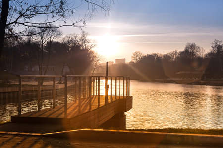 Pier on the lake in the city park. Autumn sunset, a beautiful sun path on the waterの写真素材