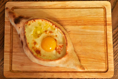 Adjar khachapuri with egg and cheese on a wooden board.の写真素材