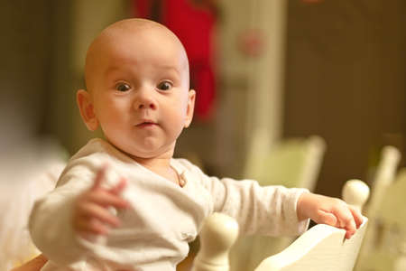 a small 5 month baby peeks out of the back of a chair in surprise.の写真素材