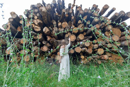 A girl stands in front of felled trees looking at them with regret. Take care and save nature. Background of cut down trees, logs in the forestの写真素材