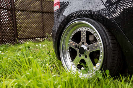 Aluminum forged wheels on the green grass in dandelions. Polish rims and bolts. Black car is on the...