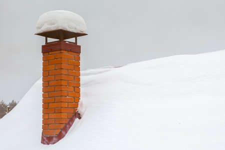 Red brick chimney with iron chimney cap on the roof in snow.の写真素材