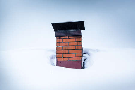 Red brick chimney with iron chimney cap on the roof in snow.の写真素材