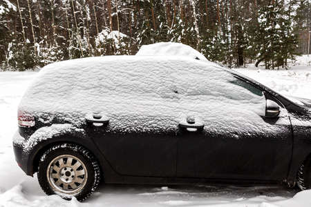 Black dirty car under the snow in forest. Frozen car in snowdrift. winter problems to start engineの写真素材