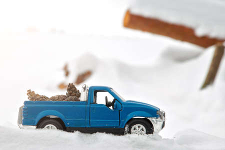 Blue toy pickup truck in sawmill. Stuck at snowdrift and sawdust. Carrying fir cones in the back of a car bodyの写真素材