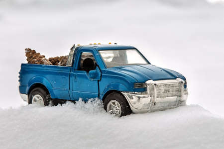 Blue toy pickup truck in sawmill. Stuck at snowdrift and sawdust. Carrying fir cones in the back of a car body.の写真素材