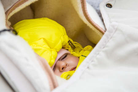Infant sleep in baby stroller in winter forest.  warmly dressed. yellow jumpsuit.の写真素材