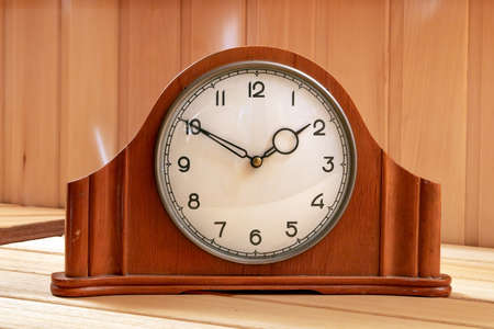 Old table clock made of wood. Mechanical. On a wooden background.
