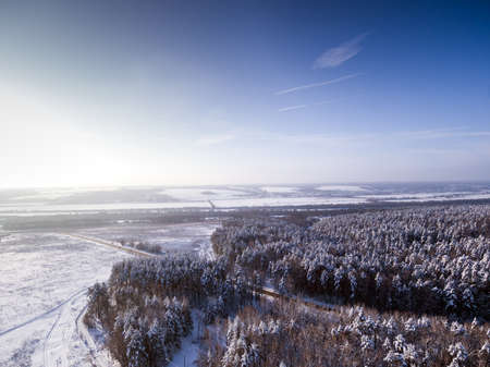 Bird's eye aerial view to road through winter forest. Frozen river on backgroundの写真素材