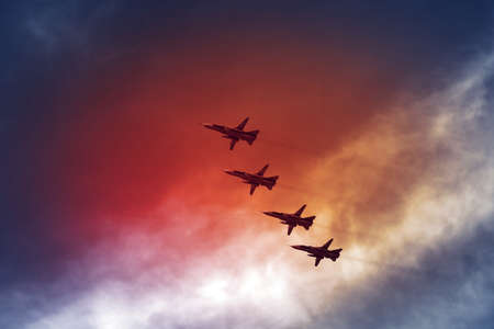 Combat aircraft fighters fly against the red fire sky. Jet squadronの写真素材