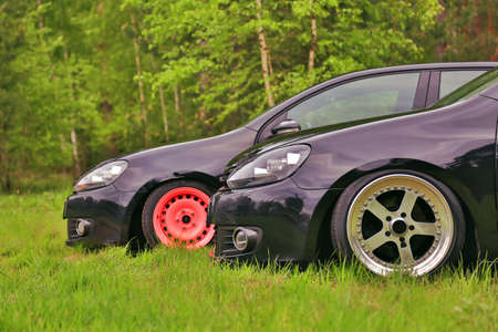 2 black cars in tuning. Parked on grass. With custom polished wheels, and living coral color wheel.の写真素材
