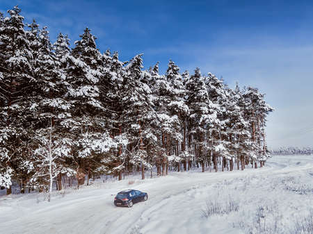 Black dirty hatchback car on winter road in the forest. Trees in snow. Aerial view.の写真素材