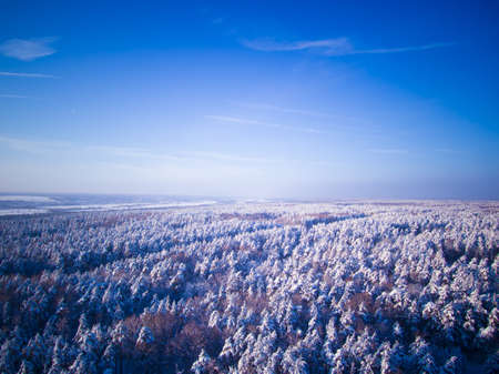Highway through the winter forest. Aerial view on road and river on background. Blue sky.の写真素材