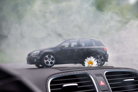 Moscow. Autumn 2018. Black toy car stays in smoke on dashboard of the same real car. Volkswagen golf...