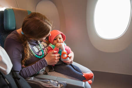 Mother carry her infant baby during flight. Sitting together near the window in airplaneの写真素材