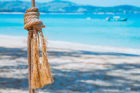 A rope with a knotted sea knot against a blue sea and sandy beach. Summer leisure at the water. Closeupの写真素材