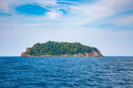 Lonely green desert island in the ocean. Calm sea and blue sky with clouds on a sunny dayの写真素材