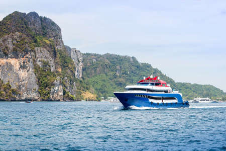 Blue with white and red accents pleasure speed boat. Sailing on the sea against a tropical island....