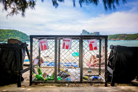 Garbage containers for separate waste collection on the tropical beach near people who sunbathing.