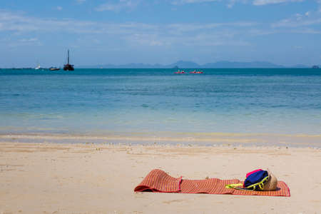 Empty mat bed on an empty sandy beach. Instead of a chaise lounge on the wild coast. Sunny weather, ships at sea on the background.