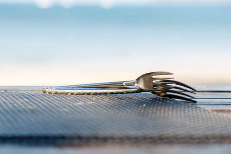 Two forks lie on top of each other. On a wooden table with bamboo mat. On the background of the sea in blur.の写真素材