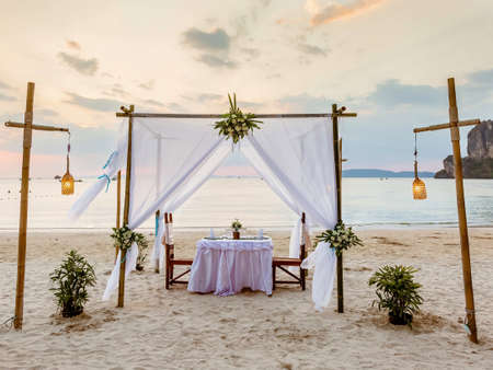 Sunset and romantic luxury dinner at tropical beach. Decorated table with vine glasses. White and magenta tonesの写真素材