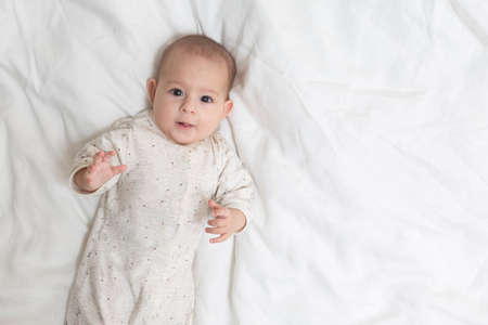 Very surprised and impressed  little baby girl lying on a white bed. Copy space at the rightの写真素材