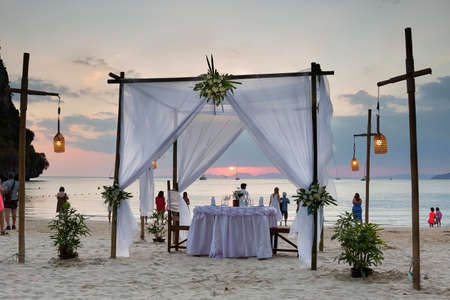 Tourists enjoy the sunset view on the beach. On the sand set table decorated for a romantic dinner. Against the background of the cliff and the sea.