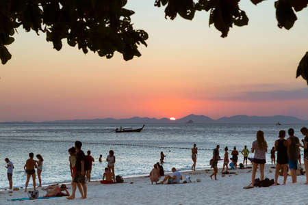 Krabi province, Thailand - February 14, 2019: A lot of tourists on the Phra nang beach enjoy the view of the sunset in the sea. Against the backdrop of the mountains, a wooden boat sails on the sea.のeditorial素材