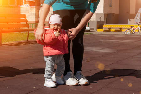 Nine month girl shows her finger. Mother holding her baby in pink by hands and teaching making first...