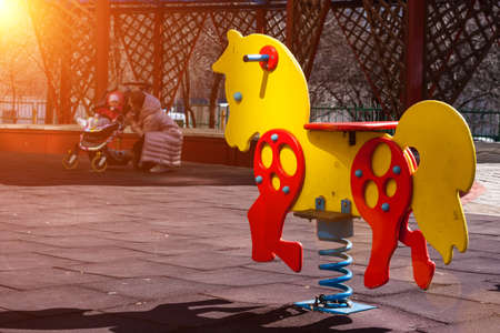 Yellow with red swing spring horse toy for kids on a children's playground. Mother with baby in...