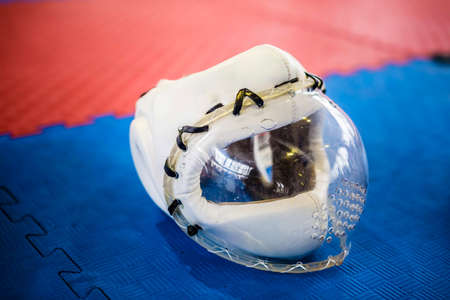 White protective helmets with clear plactic mask for martial arts on the red blue floorの写真素材