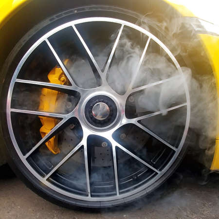Yellow car with light alloy wheels with carbon ceramic brakes and smoke from it. Close up, square...