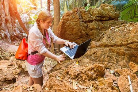 Girl travel agent. Develops a new tourist route for tourist excursions through the mountains and jungles. Works with cards in a laptop. Looks at the computerの写真素材