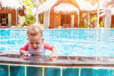 Cute little baby trying to get out of the pool.の写真素材