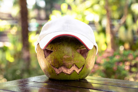 Fresh green coconut on the table. He is wearing a white baseball cap. Halloween symbols are carved...