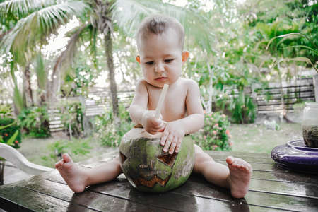 A small one-year-old child thoughtfully plays with the symbol of Halloween. Using coconut instead of pumpkinの写真素材