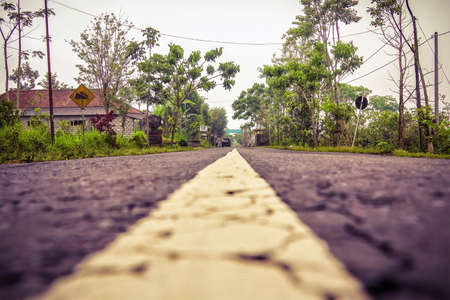 An asphalt road in Asia runs through a village. A shot from the ground. From the bottom of the markings in the center of the road.の写真素材
