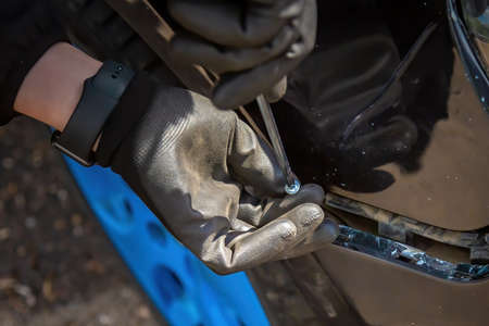 A man is trying to fix a car bumper. Screws in a screwdriver for fastening. Close-up of a hand in a...