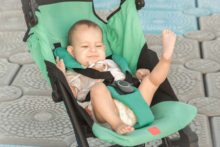 Happy one year old baby in a compact pram for traveling on the pier.